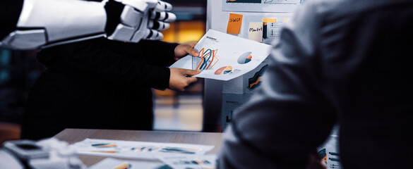A striking image of a human and robot collaborating in a modern office setting, showcasing data analysis through charts and graphs for innovative presentation techniques.Noogenesis