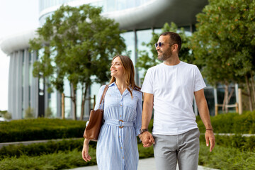 Couple enjoys a leisurely stroll hand in hand near modern architecture on a sunny day © BGStock72