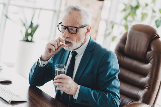 Mature businessman taking medication at work in his modern office environment during a busy workday - Powered by Adobe