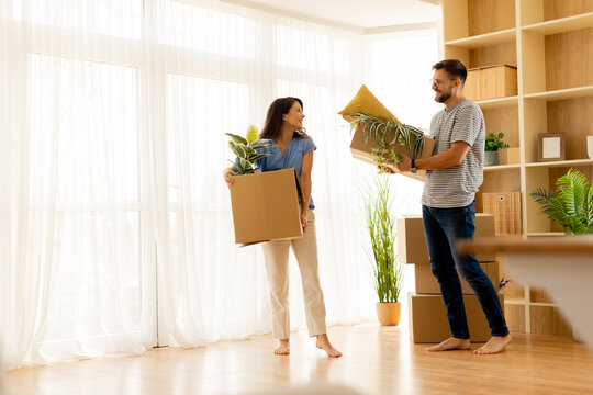 Moving day joy as couple carries boxes and plants into new apartment - Powered by Adobe