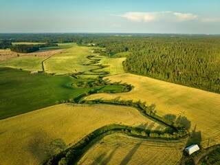 Obraz premium Aerial view of winding river through fields and forest.
