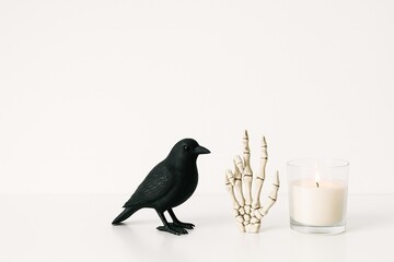 Obraz premium minimalistic halloween decor with black crow figurine, skeleton hand, and white candle on plain background