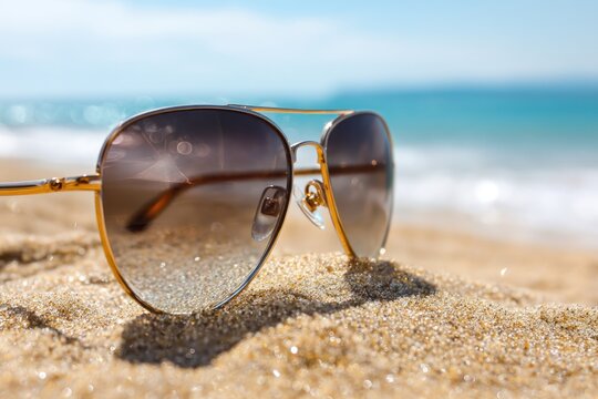 Stylish sunglasses on sandy beach with ocean view evoking summer vacation vibes
