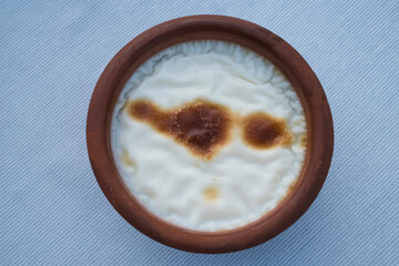 Top view of Rice pudding in a traditional clay bowl, showcasing a smooth texture with slight caramelization on the surface, set against a simple backdrop.