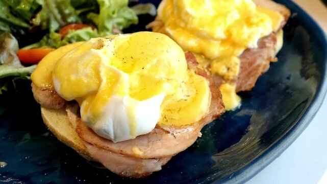 Closeup of eggs benedict with hollandaise sauce and salad on a plate