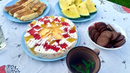 Close-up of a Fruit Jelly Cake and Chocolate Cookies. Sweet Treats on a Summer Picnic Table in a Garden