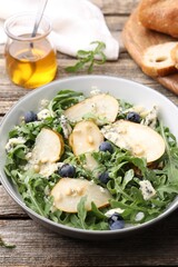 Tasty salad with arugula, pear, blue cheese, peanuts and blueberries in bowl on wooden table, closeup