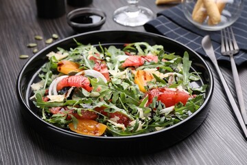 Tasty salad with arugula, cheese, grapefruit, vegetable and balsamic sauce on dark wooden table, closeup