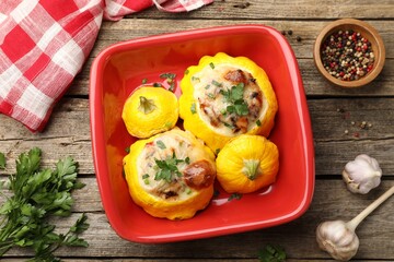 Tasty stuffed pattypan squashes in baking dish and spices on wooden table, flat lay