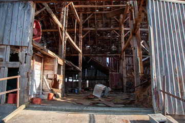 A wide-angle view of the inside of an old, deteriorating barn, showing the wooden support beams and hay loft.