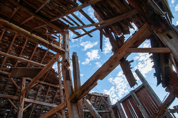 A unique perspective shot from inside a derelict barn, showing the dramatic collapse of the roof with a bright blue sky visible through the gaps.