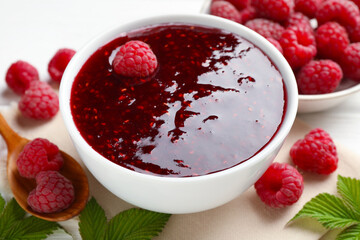 Sweet raspberry jam in bowl and berries on table, closeup