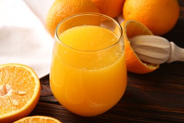 Fresh orange juice in glass, fruits and juicer on wooden table, closeup