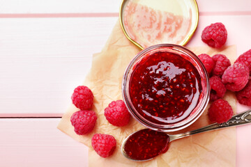 Sweet raspberry jam in glass jar and berries on pink wooden table, flat lay. Space for text