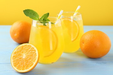 Refreshing soda water with orange slices in glasses, mint and fresh fruits on light blue wooden table, closeup
