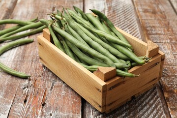 Fresh pea pods and crate on color wooden table, closeup