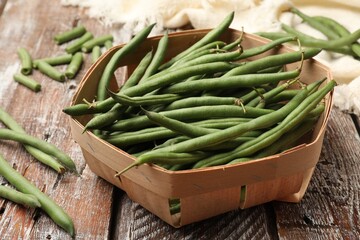 Fresh pea pods in basket on color wooden table, closeup