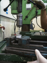 Close-up of metal drilling process using an industrial drill press machine in workshop. worker wearing protective gloves securing the workpiece in vise, demonstrating precision machining and safety