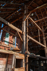 A wide-angle view of the inside of an abandoned barn, showing the intricate network of wooden beams and framing supporting the roof.
