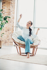 Fototapeta premium Charming young woman enjoying indoor leisure time in a cozy chair with bright lighting in a modern serene living space