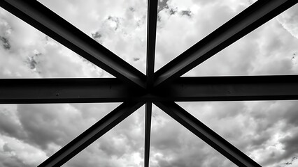 Steel beams forming geometric patterns against a cloudy sky, emphasizing industrial design.