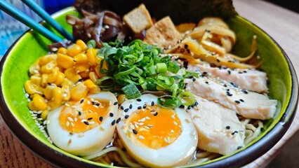 Bowl of ramen with soft boiled eggs, chicken slices, corn, green onions and sesame seeds in rich broth. Concept of Japanese cuisine, comfort food and gourmet dining