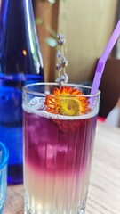 Layered lavender lemonade in a clear glass with ice and a dried flower garnish, served with a purple straw. Concept of refreshing summer drink, floral flavors and creative presentation