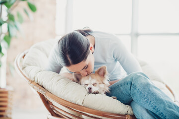 Young woman cuddling her sleeping small dog on a cozy chair in a bright living room during a peaceful day