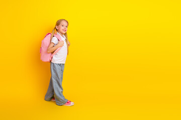 Cheerful schoolgirl wearing a pink backpack smiling against a yellow background, representing education and academic preparations