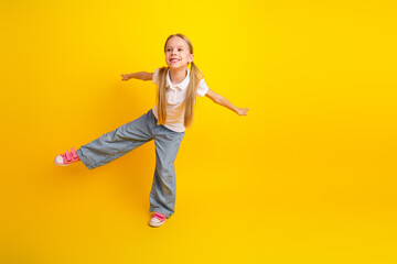 Cheerful schoolgirl posing playfully against a vibrant yellow background showcasing youthful energy and joy
