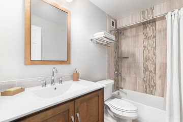 A bathroom with a natural wood cabinet, white countertop and sink, and brown tiled shower and bathtub.