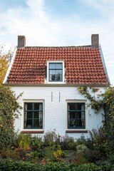 Obraz premium A lovely white house featuring a striking red roof is nestled amid lush greenery, all bathed in warm sunlight on a peaceful autumn day in a serene neighborhood