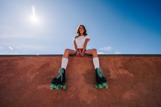 Girl with roller skates sitting on ramp under the sun