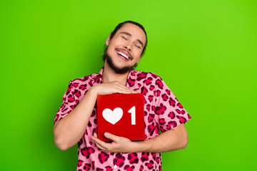 Young man holding a red box with a heart icon on a cheerful green background wearing a pink leopard print shirt