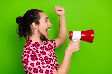 Excited young man in a stylish outfit holding a red megaphone while expressing enthusiasm and celebration, green backdrop