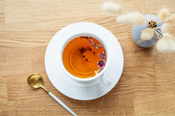 A cup of herbal tea with lemon and dry bouquet of flowers on a wooden table with spoon.