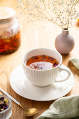 A cup of herbal tea and bouquet of flowers on a wooden table with teapot and napkin.