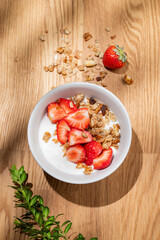Granola or muesli with natural greek yogurt, strawberry in a bowl and scattered on a wooden background