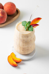 Smoothie with peach and banana in a glass on a marble stand on a light background with tropical fruits.