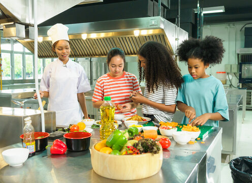 Kids children cooking group together teamwork happy fun enjoy in class learning clean culinary guid by chef supervision professional in uniform kitchen preparing food with fresh vegetables on counter.