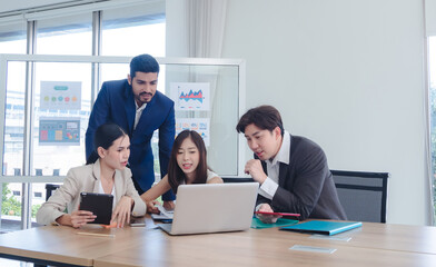Diverse group professionals meeting collaborating modern office environment team gathered around table utilizing laptop tablet discuss business strategies analyze data. background display chart graph