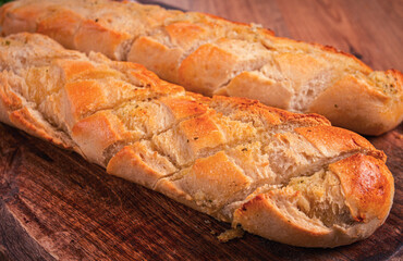 garlic bread,baguette with garlic butter and herbs, on a wooden board, with herbs and garlic cloves,