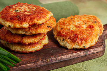 Crispy potato pancakes Latkes, stacked on a wooden board next to fresh green onions, natural light, homemade, no people,