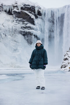 Woman Standing on Frozen River by Waterfall