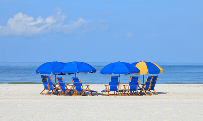 Large group of blue folding beach chairs arranged in a semi circle in front of calm blue waters.