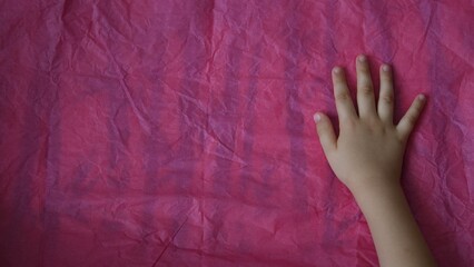 Top view of child hand touch pink crumpled paper on table with copy space