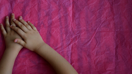 Closeup of crossed child hands on pink background with copy space