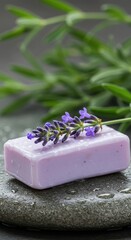 A bar of lavender soap with a lavender sprig rests on a wet stone, with green leaves in the background