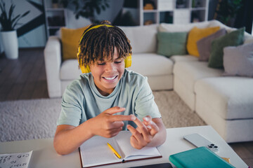 Smiling teenage boy wearing headphones studying in a cozy modern living room, demonstrating a cheerful approach to learning