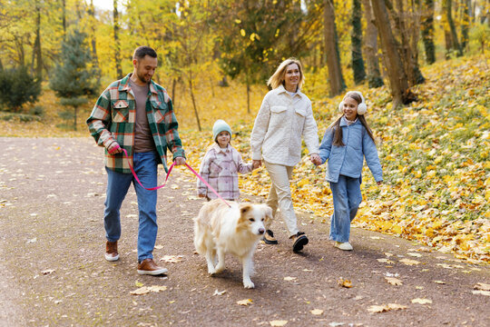 Joyful young family walking with cute dog in autumn park